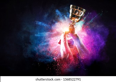 Hands holding champion cup on colourful splashes background. Mixed media - Shutterstock ID 1368522791