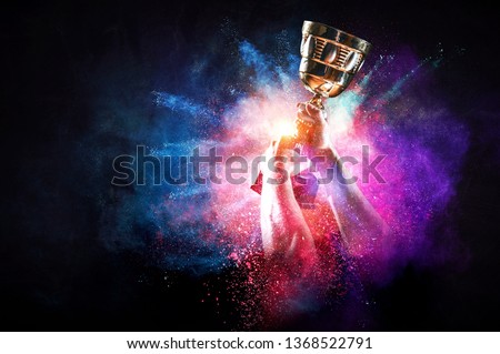 Hands holding champion cup on colourful splashes background. Mixed media