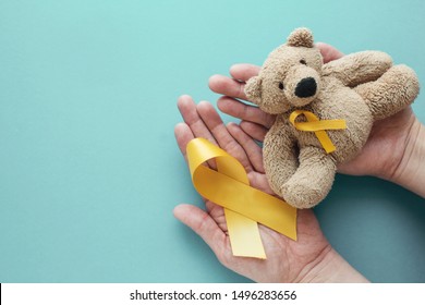 Hands Holding Children Soft Toy Brown Bear With Yellow Gold Ribbon, Childhood Cancer Awareness, September Yellow