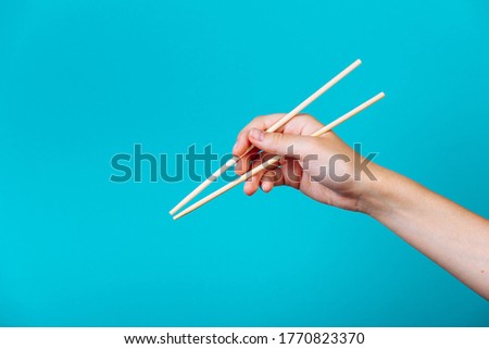 Hands holding chopsticks. Isolated on blue background, the place for caption and text