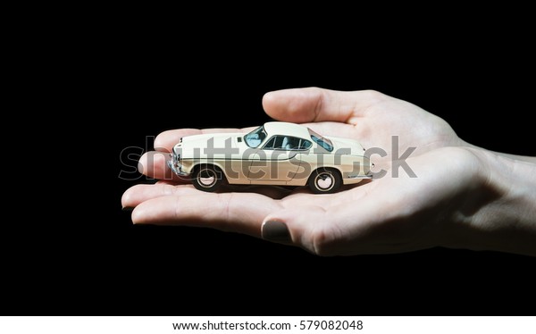 Hands holding classic retro toy car model in\
front of black background