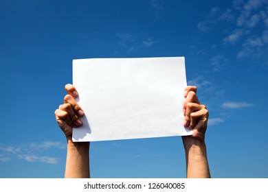 Hands Holding Clean White Sheet Paper Over The Sky.