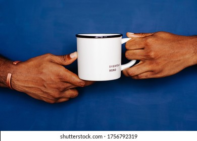 Hands Holding Coffee Mug Against The Blue Background. Everyday Hero Printed On The Mug. Frontline Worker Referral. 