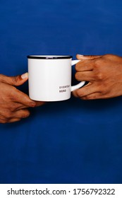 Hands Holding Coffee Mug Against The Blue Background. Everyday Hero Printed On The Mug. Frontline Worker Referral. 