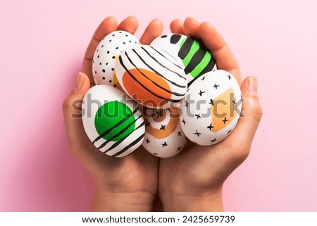 Hands holding colurfully painted easter eggs on pink background