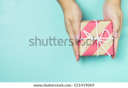 Hands holding craft paper gift box with as a present for Christmas, new year, valentine day or anniversary on blue background, top view