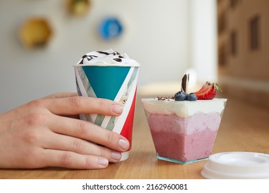 hands holding a cup of coffee with cream and chocolate in a cafe and dessert