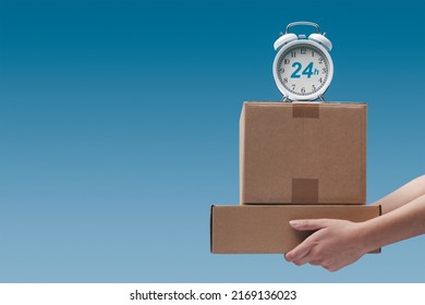 Hands holding delivery boxes and alarm clock: 24 hours delivery service, blank copy space