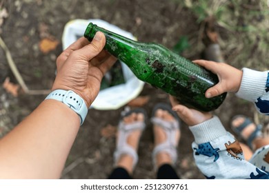 Hands holding dirty glass bottle during outdoor cleanup activity, promoting environmental awareness and recycling. Concept of family involvement in eco-friendly actions and sustainability. High - Powered by Shutterstock