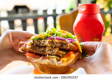 Hands holding a double cheeseburger. Hamburger food concept. Meat, salat, chesse and bread.