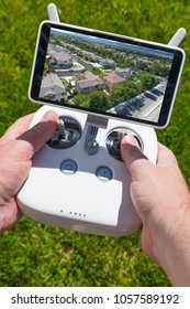 Hands Holding Drone Quadcopter Controller With Residential Homes on Screen.
