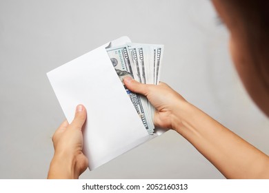 Hands holding envelope with dollar money on white background. Woman hand takes out money from an envelope, close-up. Bribe corruption, salary, earning and savings concept 