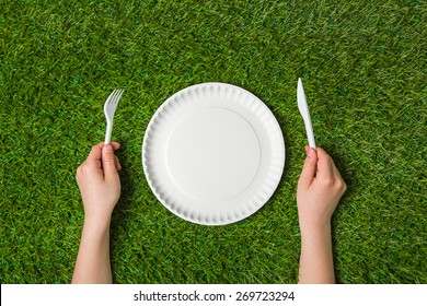 Hands holding fork and knife with plate on grass