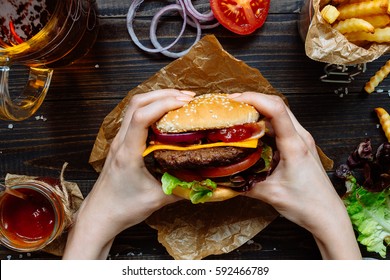 Hands holding fresh delicious burgers with french fries, sauce and beer on the wooden table top view. - Shutterstock ID 592466789
