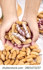 Hands holding fresh peanuts in shells with purple striped beans visible inside, surrounded by scattered peanuts from Yunnan plateau harvest