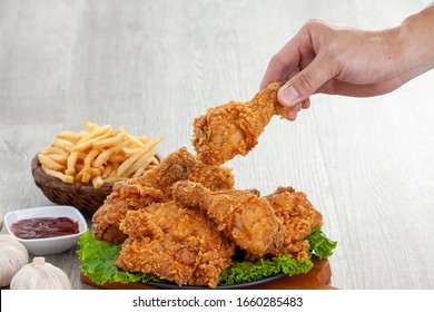 hands holding fried chickens, crispy and golden with french fries and sauce on wood table