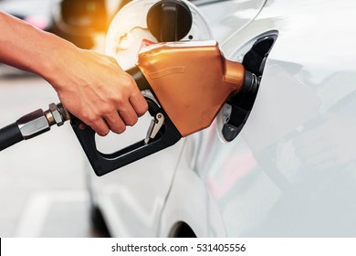 Hands holding a fuel nozzle on cars.