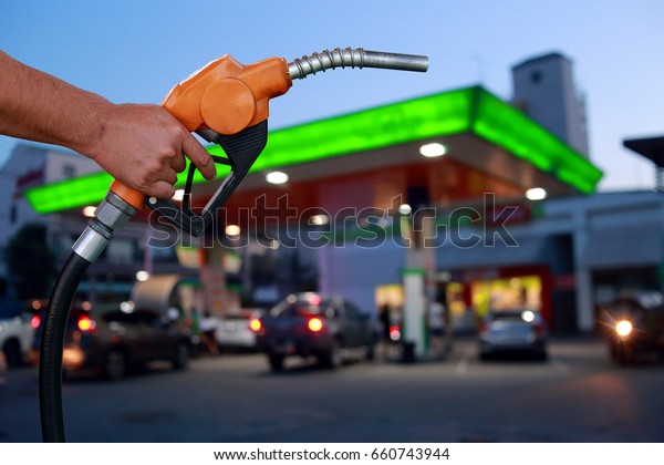 Hands holding a fuel\
nozzle on cars and blurred image of gas station with car refueling\
at night background.