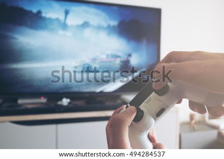 Hands holding the game controller while man playing game on TV in a room
