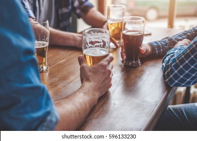 Hands holding glasses with beer on a table. - Powered by Shutterstock