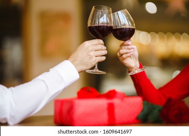 Hands holding glasses of wine on restaurant background. Couple clink glasses with red wine. Romance at restaurant for Valentine's Day- concept. Relationship & Birthday concept.