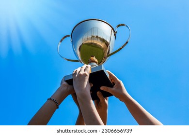 Hands holding a golden cup trophy against a blue sky with sunbeams, victory success  scholl team concept - Powered by Shutterstock