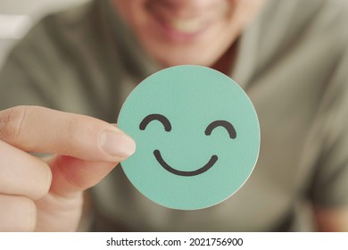 Hands holding green happy smile face paper cut, good feedback rating and positive customer review,experience, satisfaction survey,mental health assessment,feeling good,world mental health day