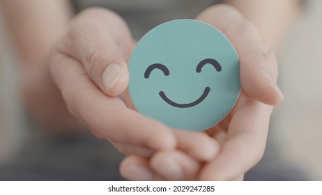 Hands holding green happy smile face, good feedback rating and positive customer review,experience, satisfaction survey,mental health assessment,child feeling good,world mental health day, Compliment  - Shutterstock ID 2029247285