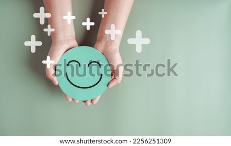 Hands holding green happy smile face, good feedback rating, positive customer review, experience, satisfaction survey, smiley mental health, child wellness, world mental health day on green background