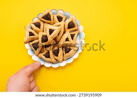 Hands holding Hamantaschen cookie isolate on yellow background. Jewish triangular filled pocket pastry associated with the Jewish holiday of Purim 2026