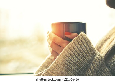 hands holding hot cup of coffee or tea in morning sunlight - Powered by Shutterstock