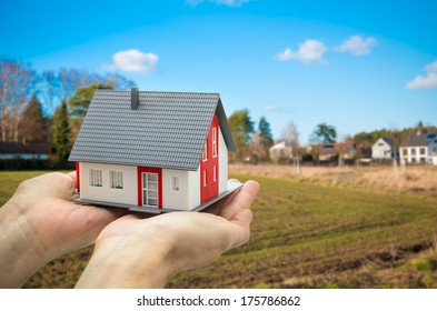 Hands holding a house model against building ground background