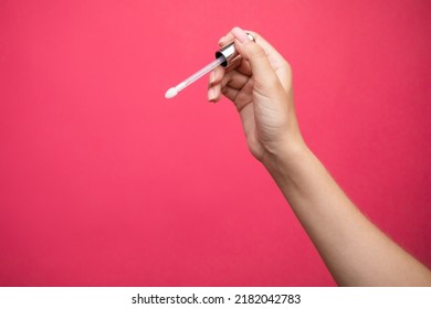 Hands Holding Lip Gloss Applicator On Pink Background.