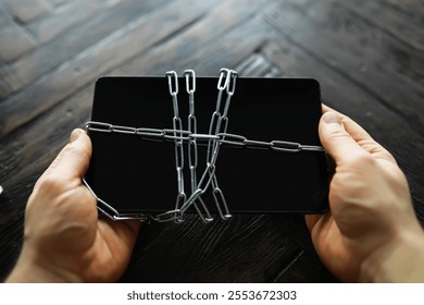 Hands Holding Locked Tablet with Chains on Dark Wooden Surface - Cybersecurity and Data Protection Concept
