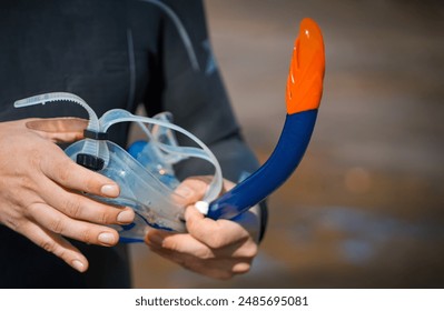 Hands holding a mask and snorkeling tube, a man in a diving suit is preparing to swim and snorkel in the ocean with diving equipment and enjoy the beauty of the underwater world, close-up view. - Powered by Shutterstock