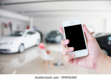 Hands Holding Mobile Phone With New Cars In Showroom Dealership