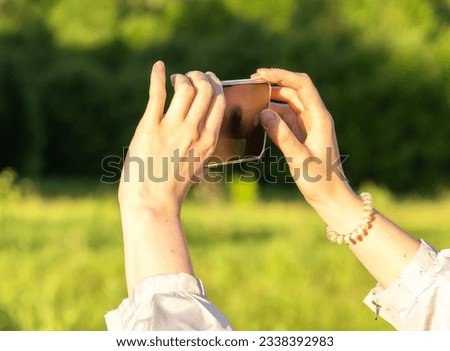 Hands holding mobile phone, taking photo, recording video in nature.