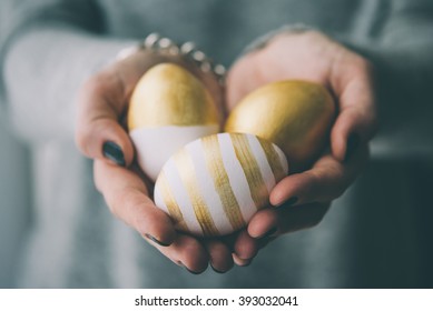 Hands holding modern  easter eggs painted in gold. Toned picture