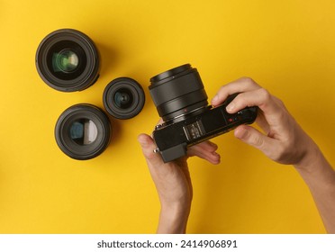 Hands holding a modern mirrorless camera with lenses on yellow background