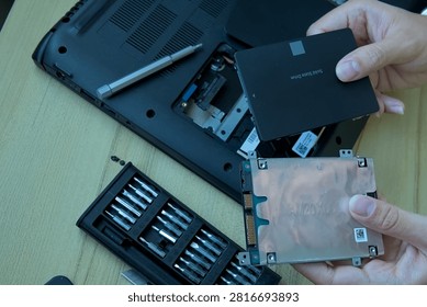 Hands holding a new 2.5-inch Solid State Drive (SSD) next to an old internal mechanical hard drive (HDD) over an open laptop chassis. Perfect visual representation of upgrading from a slow HDD to a fast SSD for better PC performance.