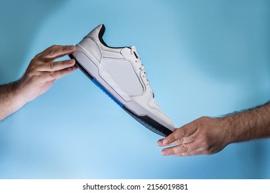 Hands Holding New Unbranded Tennis Shoes On Blue Background. New Unbranded Sneakers Or Trainers - Men's Sport Footwear. Pair Of Sport Shoes.