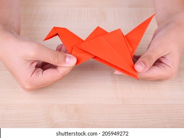 Hands Holding Origami Crane On Wooden Table