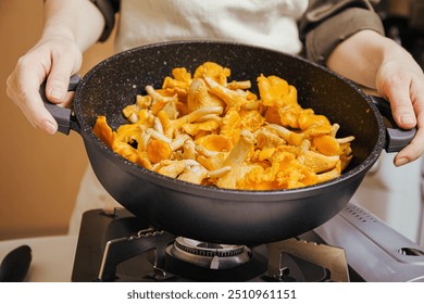 Hands holding pan filled with fresh chanterelle mushrooms, cooking on gas stove, preparing healthy vegetarian meal - Powered by Shutterstock