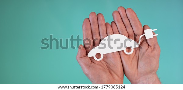 Hands holding a paper electric car on\
turquoise color background; Concept of eco friendly\
car