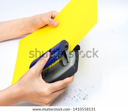 Hands holding paper hole puncher of office stationery and punching paper on white background