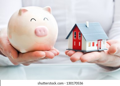 Hands Holding A  Piggy Bank And A House Model. Housing Industry Mortgage Plan And Residential Tax Saving Strategy