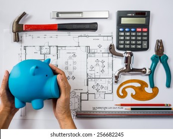 Hands Holding Piggy Bank Over Architecture  Drawing, Planning For  Home Remodel /  Saving Concept