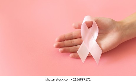 Hands holding pink ribbon on pink background, Breast cancer awareness and October Pink day, world cancer day, national cancer survivor day. - Shutterstock ID 2156997171