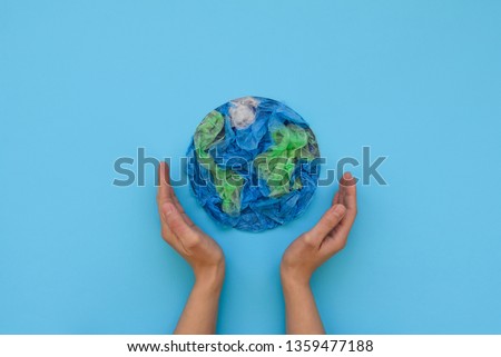 Hands holding planet Earth made from plastic disposable packages on blue background. Save the world, creative, environment pollution or World Earth Day concept. Top view