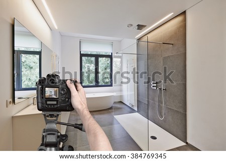 Hands holding a professional camera on tripod taking picture in  tiled bathroom with windows towards garden